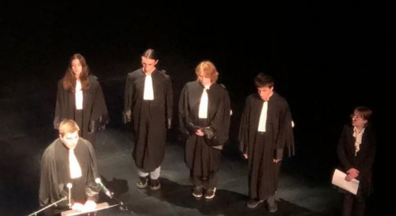 6 lycéens du lycée Châtelet de Saint-Pol-sur-Ternoise se tiennent sur une scène en habit d'avocat, l'un d'eux parle au micro