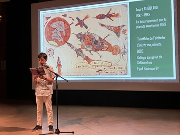 Un élève lit un extrait de texte à voix haute devant un écran qui projette une oeuvre d'art