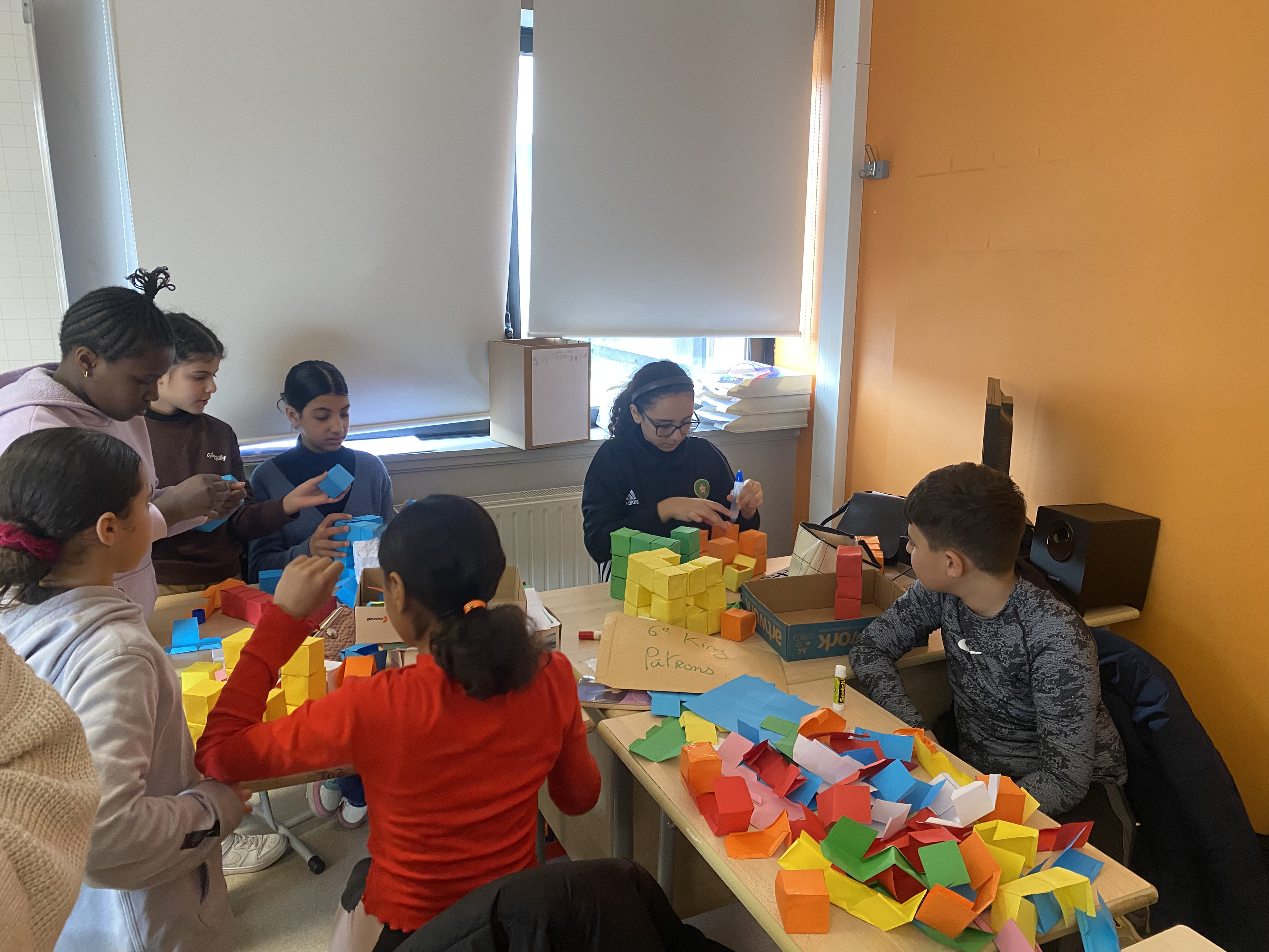 Plusieurs élèves sont réunis autour d'une table pour construire des cubes avec des feuilles de papier colorées