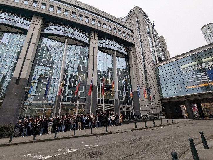 Des élèves se trouvent devant le parlement européen, devant lequel sont présents de nombreux drapeaux des pays de l'Union Européenne