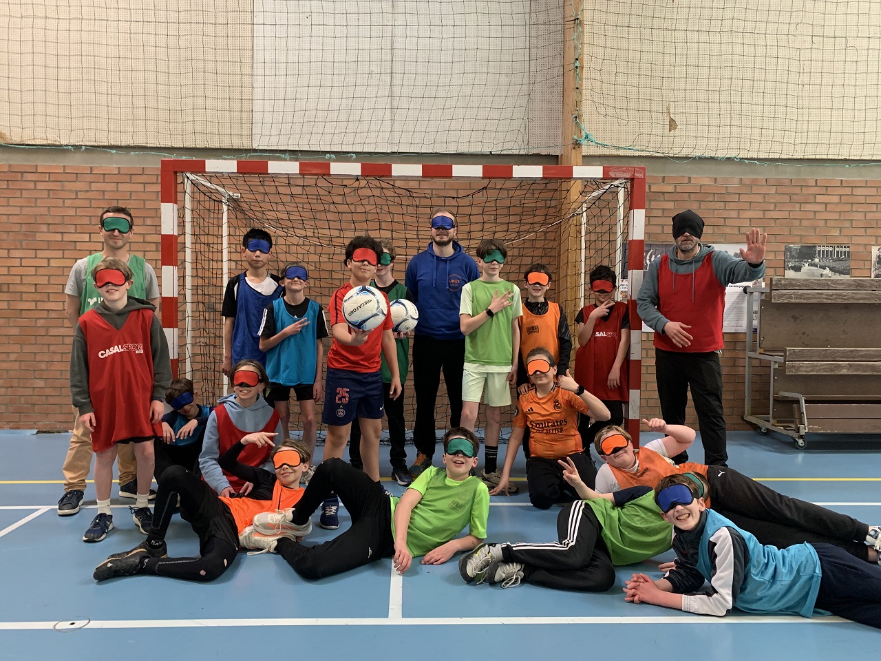 Des élèves en habits de sport se tiennent devant une cage de foot, ils ont tous les yeux bandés