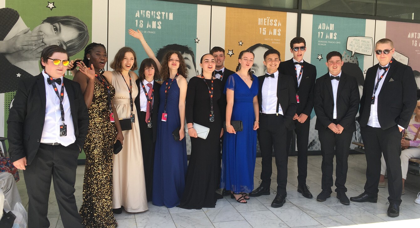 Les élèves lauréats du concours Moteur! se tiennent devant les affiches officielles du concours avant leur montée des marches au festival de Cannes
