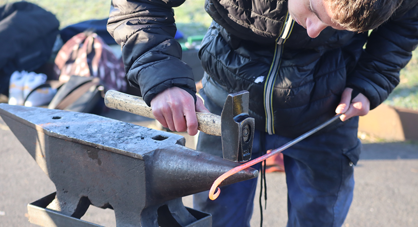Un collégien découvre la ferronnerie en réalisant une boucle avec une tige de métal et un marteau sur une enclume