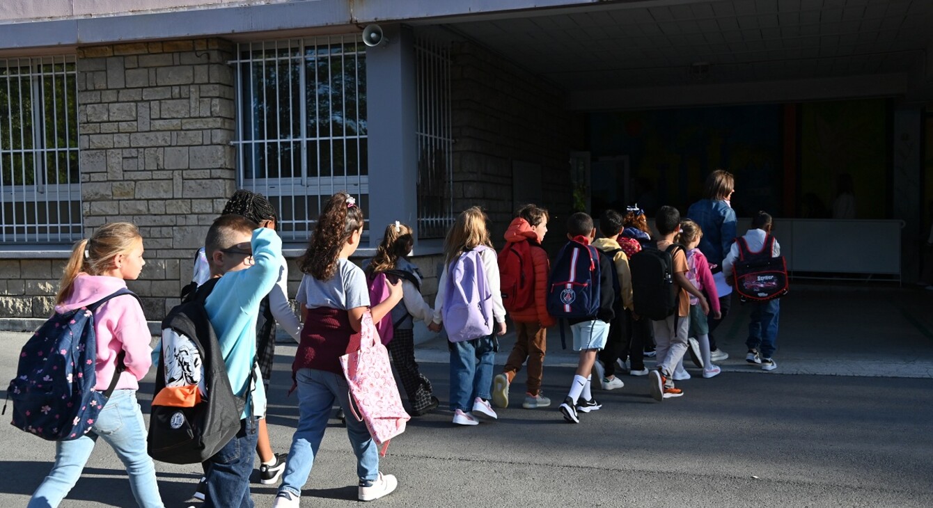 Des enfants rangés deux par deux suivent leur enseignante pour rentrer en classe