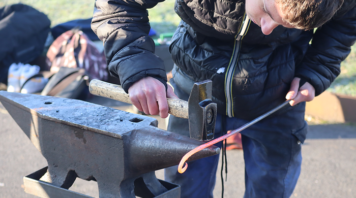 Un collégien découvre la ferronnerie en réalisant une boucle avec une tige de métal et un marteau sur une enclume