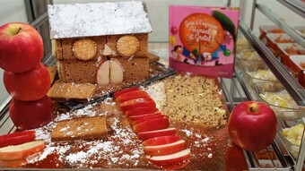 Photo d'une maison en pain d'épices fabriquée par la cantine du collège Gabriel de la Gorce à Hucqueliers à côté d'un livre avec les personnages Hansel et Gretel