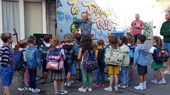 Plusieurs élèves avec leurs sacs sur le dos se trouvent dans une cour d'école et regardent une marionette en forme de dragon