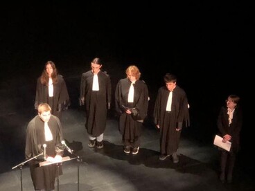 6 lycéens du lycée Châtelet de Saint-Pol-sur-Ternoise se tiennent sur une scène en habit d'avocat, l'un d'eux parle au micro